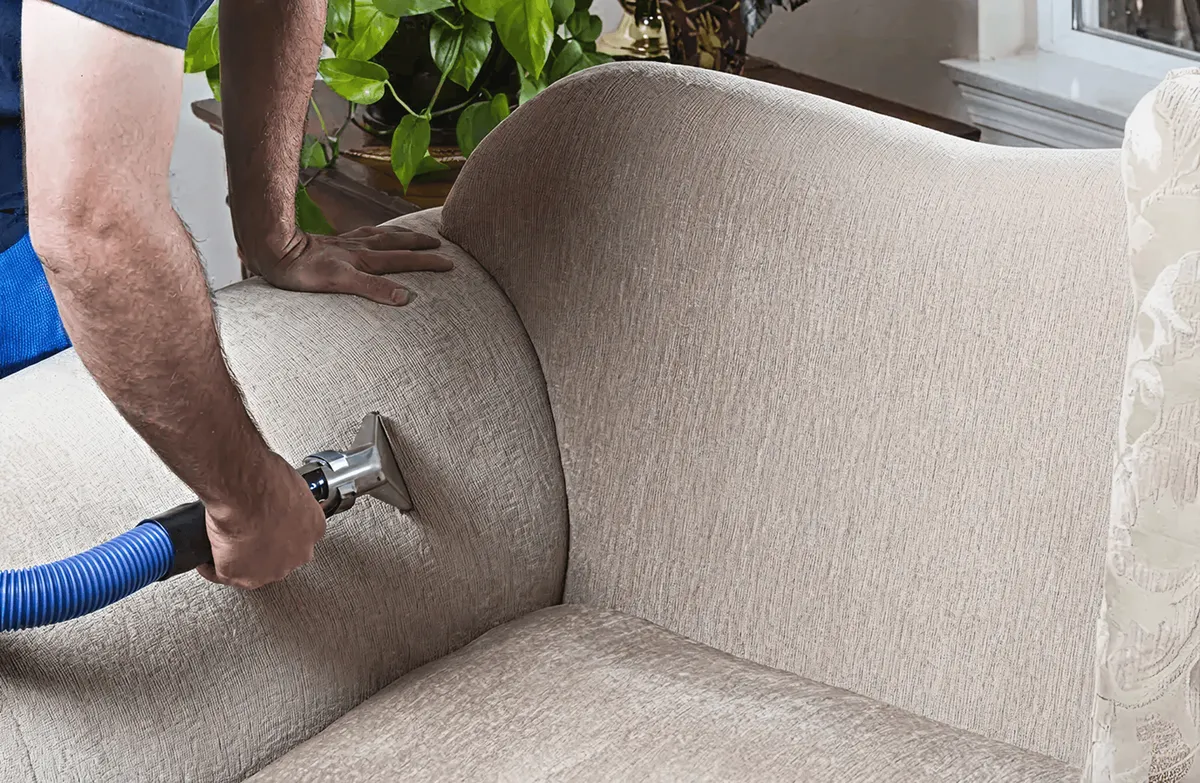 Professional upholstery cleaner deep-cleaning a fabric sofa with a handheld extraction tool and hose, Tampa, FL.